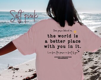 May include: A soft pink t-shirt with the text "Dear person behind me, the world is a better place with you in it. Love from, the person in front of you" and "Suicide Prevention Awareness".