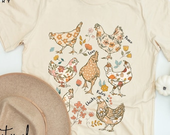 May include: A beige t-shirt with a graphic of chickens with floral patterns and the words "Love", "Peace", "Rules", "Chicks" and "Natural".