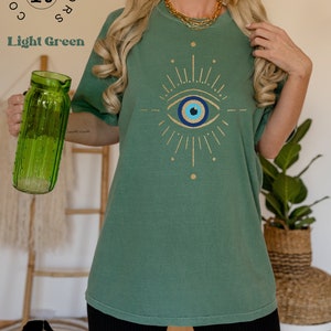May include: A light green t-shirt with a gold glitter evil eye design. The shirt is a relaxed fit and has a crew neck.