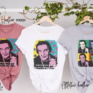 May include: Three t-shirts with a pop art style image of a woman with a quote about authority. The t-shirts are in heather mauve, white, and athletic heather.