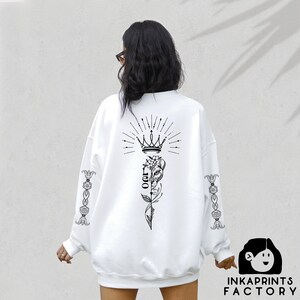 May include: White sweatshirt with a black graphic design on the back. The design features a crown, a flower, and the word "Leo". The sleeves have a floral design.
