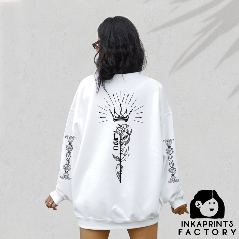 May include: White sweatshirt with a black graphic design on the back. The design features a crown, a flower, and the word "Leo". The sleeves have a floral design.
