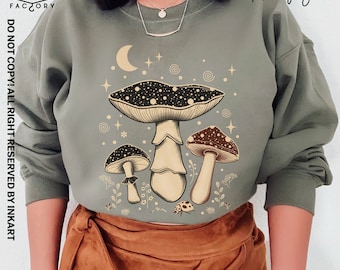 May include: A green sweatshirt with a graphic of three mushrooms and a crescent moon. The mushrooms are black and white with brown stems. The moon is white with a yellow crescent shape. The text "Military green" is in the upper right corner of the image.