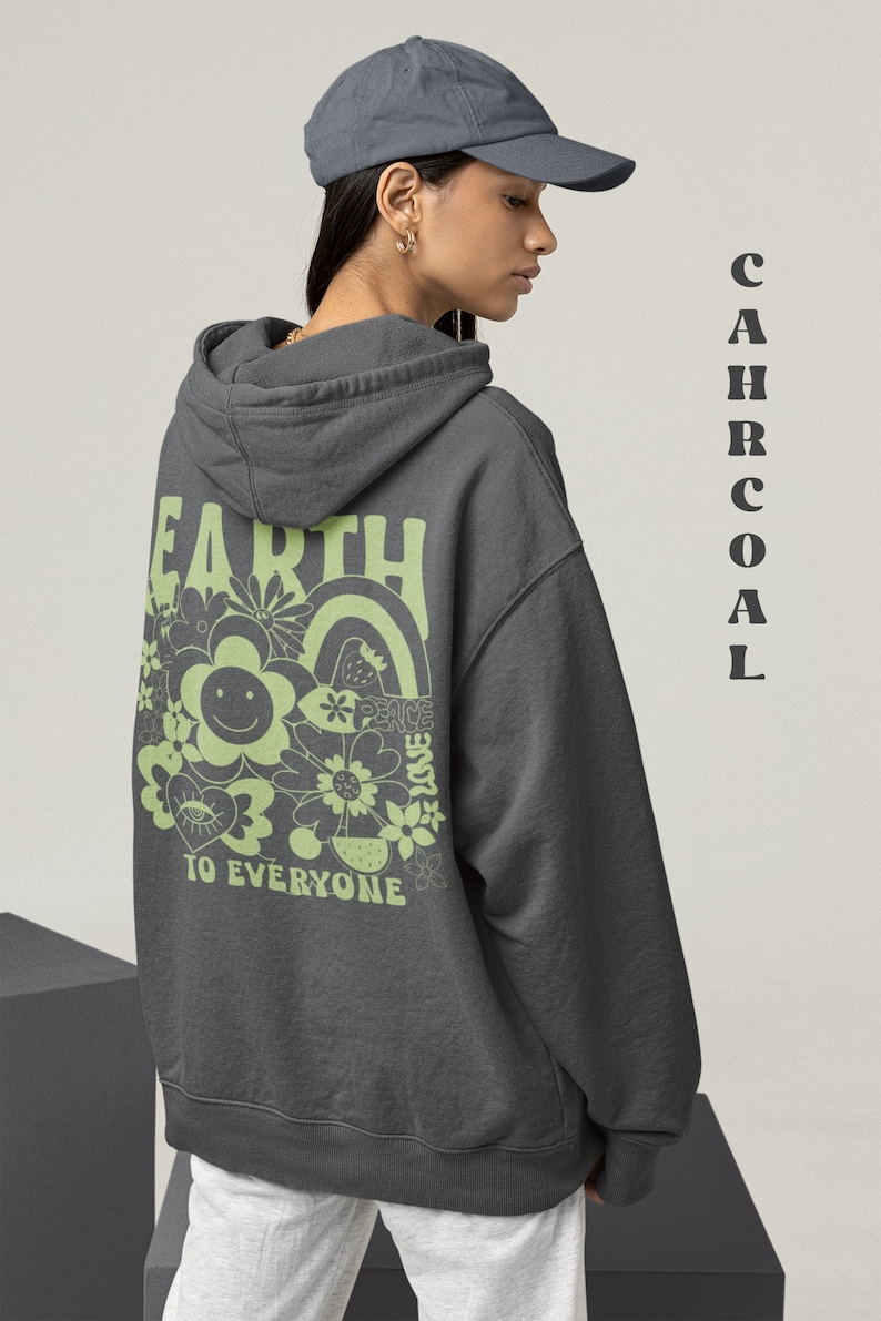 May include: A charcoal gray hooded sweatshirt with a green graphic print on the back. The graphic features the word "Earth" in a retro font, surrounded by flowers, a rainbow, and the words "Peace, Love, To Everyone".