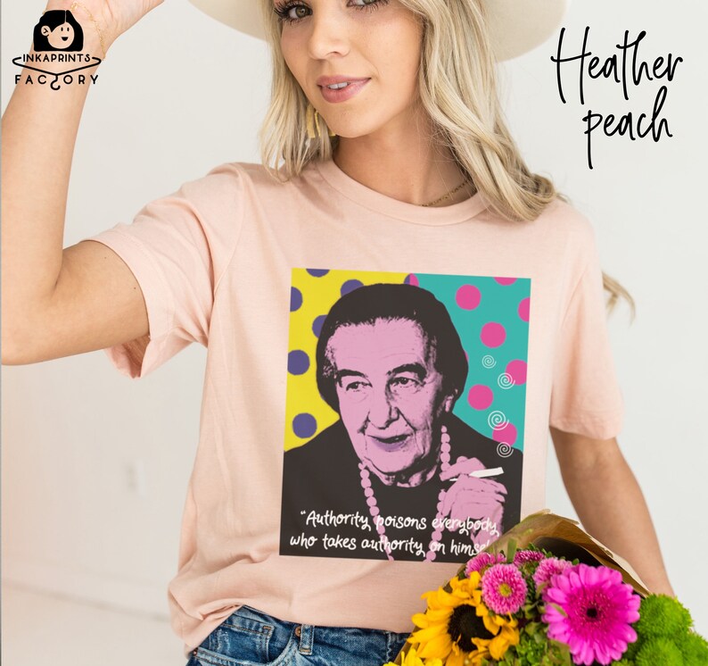 May include: A pink t-shirt with a graphic of a woman with a quote that reads "Authority poisons everybody who takes authority on himself". The graphic is in a pop art style with colorful dots and swirls.