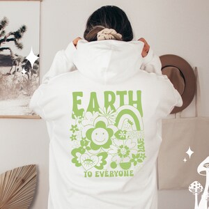 May include: White hoodie with a green graphic print on the back that says "EARTH TO EVERYONE" with a flower and rainbow design.