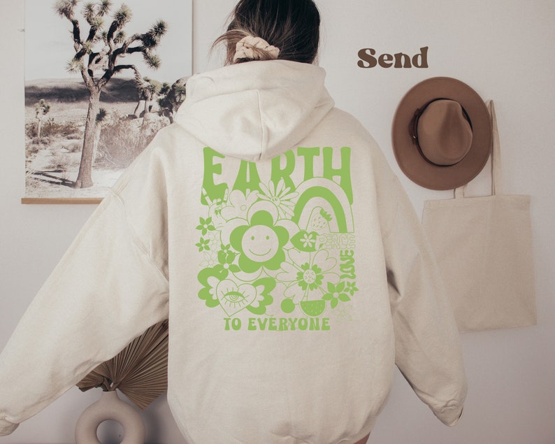 May include: A cream-colored hoodie with a green graphic on the back that says "Earth to Everyone" with a flower, rainbow, and other designs.