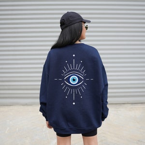 May include: A navy blue sweatshirt with a white evil eye design on the back. The evil eye is a symbol of protection against negative energy.