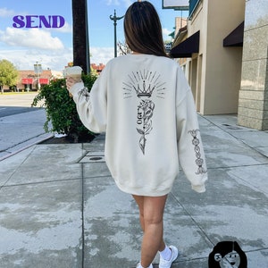 May include: A white sweatshirt with a black graphic print of a crown, a flower, and the word "OG" on the back. The sweatshirt has a black floral design on the sleeve.