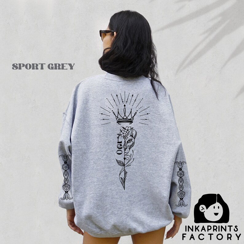 May include: A gray sweatshirt with a black graphic print of a crown, a flower, and the word "OOR" on the back. The sleeves have a black floral design. The sweatshirt is called "Sport Grey".