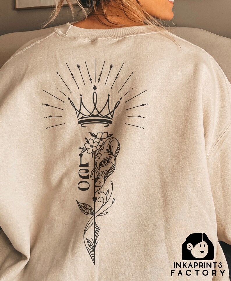 May include: A beige sweatshirt with a black graphic design on the back. The design features a crown, a lion's face, and the word "Leo" in a stylized font.