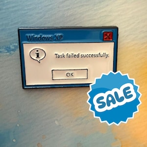 May include: A blue and white enamel pin depicting a Windows XP error message. The text reads "Windows XP", "Task failed successfully." and an "OK" button. A blue "SALE" sticker is in the bottom right corner.