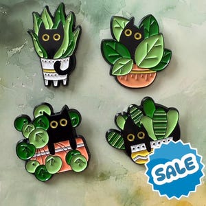 May include: Four enamel pins depicting black cats in plant pots. The pins show black cats amongst green leaves and pots in orange, white, and black. One pin includes a blue "SALE" sticker.