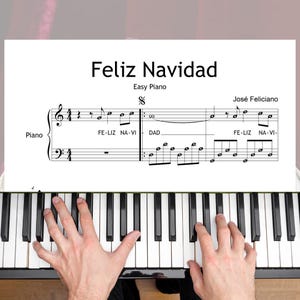 Op de afbeelding: Muziekblad voor "Feliz Navidad" voor eenvoudige piano, met de naam van de componist, José Feliciano. Het muziekblad ligt op een pianoklavier, met de handen van de pianist zichtbaar.