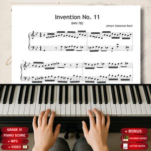Op de afbeelding: Een bladmuziekpagina getiteld Invention No. 11 BWV 782 van Johann Sebastian Bach boven een pianotoetsenbord. De partituur bevat zwarte muzieknotatie op een witte achtergrond. Rode rechthoekige labels onderaan geven bonusfuncties aan.