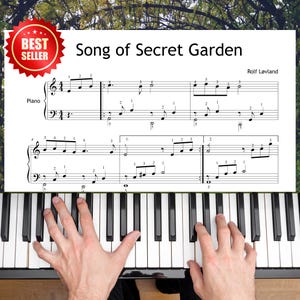 Può includere: Uno spartito per pianoforte intitolato "Song of Secret Garden" di Rolf Løvland, con un adesivo "Best Seller". I tasti del pianoforte sono bianchi e neri e le mani di una persona suonano il pianoforte. Lo spartito è in bianco e nero.
