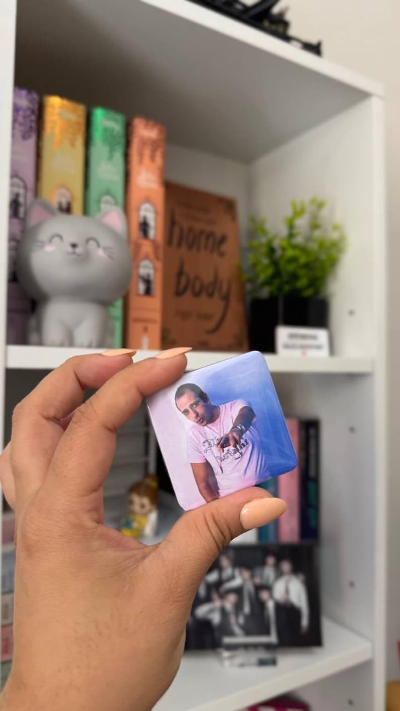 Puede incluir: Una chapa cuadrada con una impresi&oacute;n fotogr&aacute;fica de una persona con una camiseta rosa claro con texto oscuro, se&ntilde;alando hacia adelante con una mano. La chapa tiene un acabado brillante, esquinas redondeadas y un fondo azul y blanco.