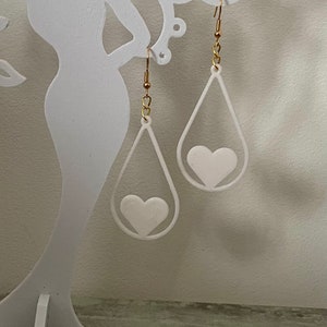 May include: A pair of white teardrop-shaped earrings with a white heart cutout in the center of each earring.