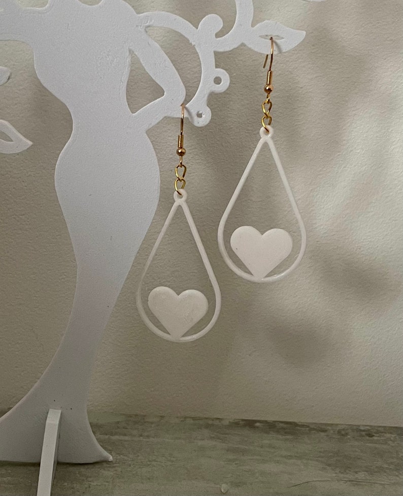 May include: A pair of white teardrop-shaped earrings with a white heart cutout in the center of each earring.