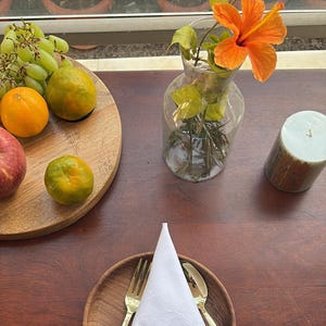 May include: White linen napkin with a blue embroidered letter 'S' and scalloped edges. The napkin is folded and placed on a wooden plate with gold silverware.