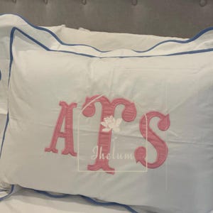 May include: White pillowcase with a blue trim and pink embroidered letters "ATS" on the front.