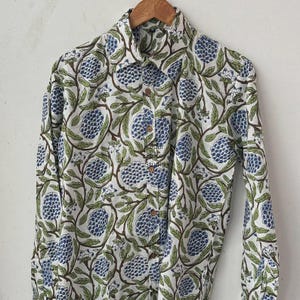 May include: White button-down shirt with a floral pattern. The shirt features a repeating design of blue flower clusters, green leaves, and brown stems. The shirt is made of a lightweight fabric and has a classic collar and long sleeves.