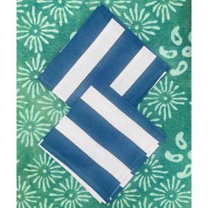 May include: Two square blue and white striped cloth napkins are stacked on a green patterned surface. The napkins have thick, bold white stripes against a blue background. The green surface has a floral design.
