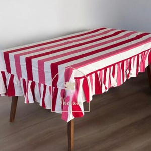 May include: A rectangular tablecloth with alternating red, white, and pink stripes. The tablecloth has a ruffled edge and is draped over a wooden table. The text "The um" is visible on the tablecloth.