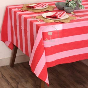 May include: A red and pink striped tablecloth covers a wooden table. The table is set with plates, napkins, and placemats. The overall theme is a dining setting.