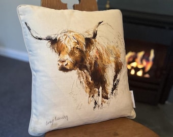 May include: A cream-colored throw pillow with a watercolor illustration of a brown Highland cow. The pillow has a subtle linen texture and the artist's signature "Lucy Redding" is visible in the bottom left corner.