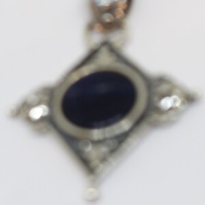 May include: A silver pendant with a dark blue oval gemstone surrounded by smaller clear gemstones. The pendant is in the shape of a diamond.
