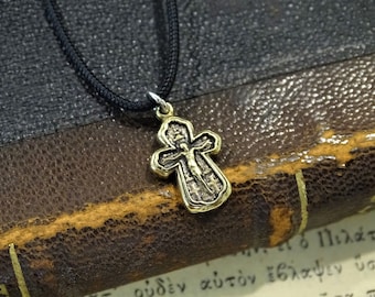 May include: A gold and silver cross pendant with a black cord necklace. The cross features a detailed design of a figure on the cross.