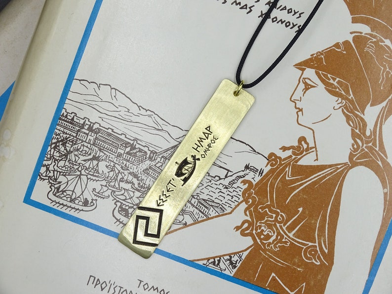 May include: A gold-coloured metal bookmark with an inscription in Greek. The bookmark features a stylised ship design and the text "&Epsilon;&Sigma;&Sigma;&Epsilon;&Tau;&Iota; &Eta;&Mu;&Alpha;&Rho; &Omicron;&Iota;&Nu;&Kappa;&Rho;&Omicron;&Sigma;". The bookmark is hanging from a black cord.