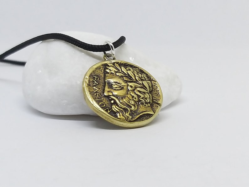 May include: A gold-colored necklace with a round pendant featuring a detailed profile of a man with a laurel wreath and the inscription "PANEION".