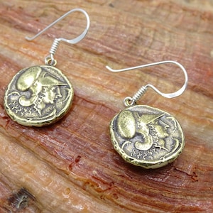 May include: A pair of gold-toned earrings featuring a detailed design of a head in profile. The earrings are made of metal and have a hook closure.