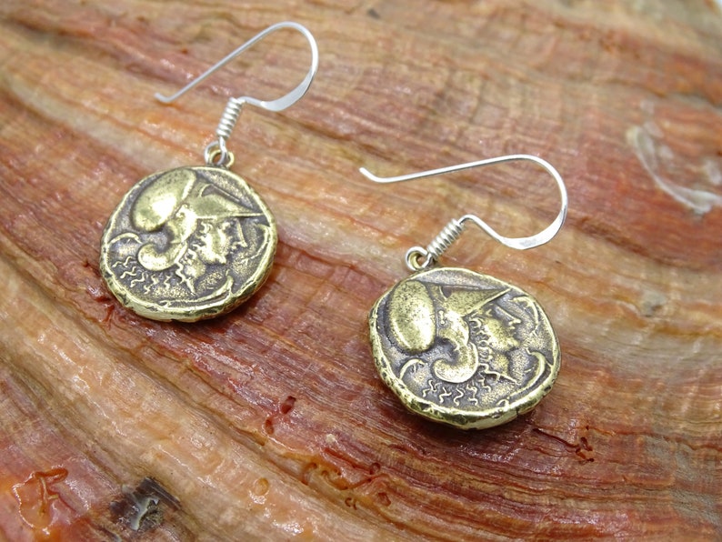 May include: A pair of gold-toned earrings featuring a detailed design of a head in profile. The earrings are made of metal and have a hook closure.