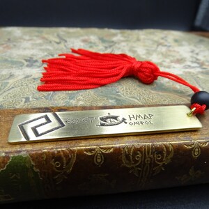 May include: A brass bookmark featuring a Greek key design and the text "&Theta;&Epsilon;&Sigma;&Sigma;&Alpha;&Lambda;&Omicron;&Nu;&Iota;&Kappa;&Eta;" and "&Eta;&Mu;&Alpha;&Rho; &Omicron;&Mu;&Eta;&Rho;&Omicron;&Sigma;". The bookmark has a red tassel with a black bead.