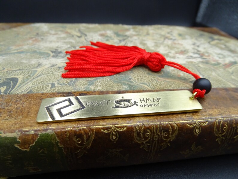 May include: A brass bookmark featuring a Greek key design and the text "&Theta;&Epsilon;&Sigma;&Sigma;&Alpha;&Lambda;&Omicron;&Nu;&Iota;&Kappa;&Eta;" and "&Eta;&Mu;&Alpha;&Rho; &Omicron;&Mu;&Eta;&Rho;&Omicron;&Sigma;". The bookmark has a red tassel with a black bead.