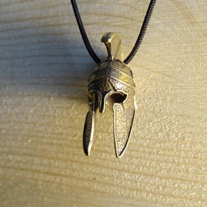May include: A bronze pendant in the shape of a Roman helmet with a black cord.
