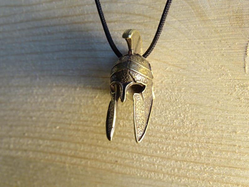 May include: A bronze pendant in the shape of a Roman helmet with a black cord.