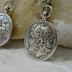 May include: Two silver-toned pendants with chain links. One pendant features a profile of a man with a beard and a laurel wreath. The other pendant features a horse and rider.