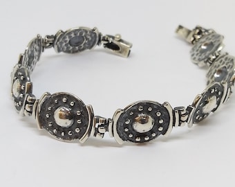 Könnte beinhalten: Ein silbernes Armband mit einem Kettenglieddesign und runden, strukturierten Silberanhängern. Die Anhänger haben eine erhabene Mitte und eine gehämmerte Oberfläche.
