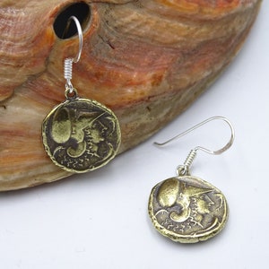 May include: A pair of gold-toned earrings with a coin-shaped design featuring a profile of a woman's face. The earrings have silver hooks.