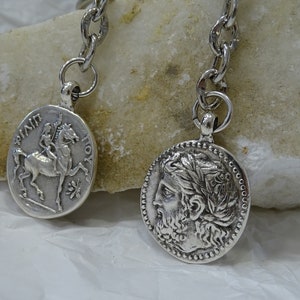 May include: Silver key chain with two round pendants. One pendant features a depiction of a rider on horseback with the text "&Pi;&Iota;&Nu;&Delta;&Alpha;&Rho;&Omicron;&Sigma;" and "&Iota;&Omicron;&Upsilon;&Sigma;". The other pendant features a profile of a man with a laurel wreath.