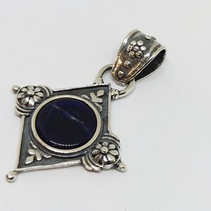 May include: A silver pendant with a dark blue gemstone set in a diamond-shaped frame with ornate floral details.