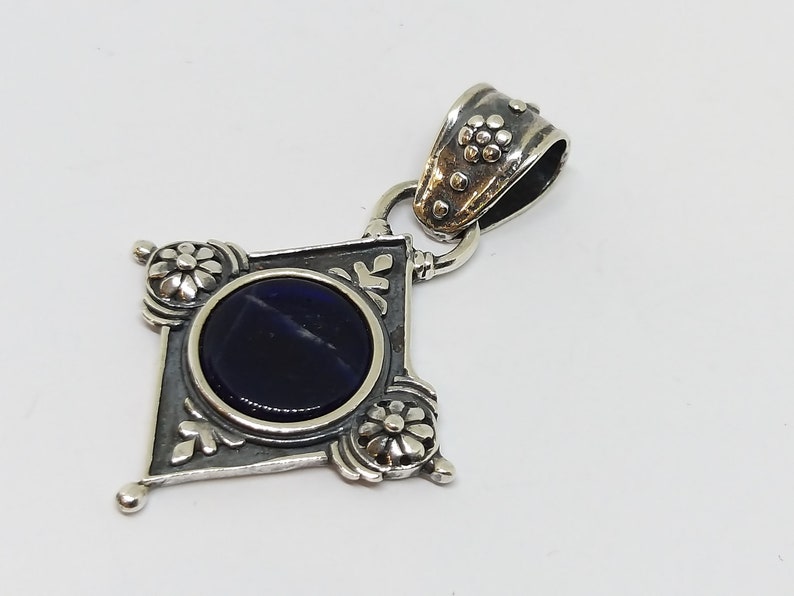 May include: A silver pendant with a dark blue gemstone set in a diamond-shaped frame with ornate floral details.