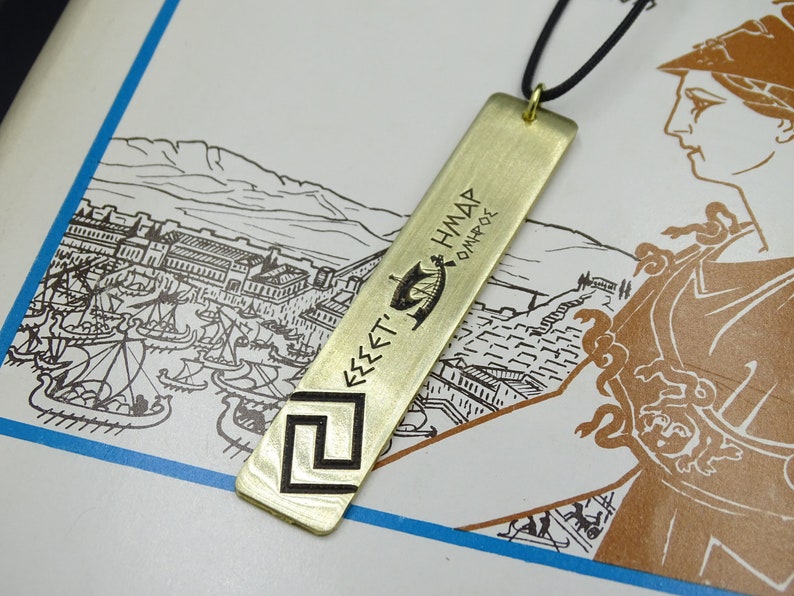May include: A gold-coloured metal pendant necklace with a rectangular tag featuring an engraved image of a ship and the text "&Epsilon;&Sigma;&Sigma;&Epsilon;&Tau;' &Eta;&Mu;&Delta;&Alpha;&Rho; &Omicron;&Mu;&Eta;&Rho;&Omicron;&Sigma;".