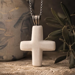 May include: A white stone cross pendant with rounded edges suspended from a silver-toned metal box chain. The pendant features a smooth, matte finish and is attached to the chain by a silver-toned metal bail stamped with the number 925.