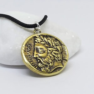 May include: A gold-toned pendant necklace with a round coin-shaped charm featuring a detailed profile of a man's face with a laurel wreath. The inscription "PANEION" is visible on the charm.