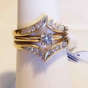 May include: A gold ring set with a large, round, clear diamond. The ring is made up of three bands, each with a row of smaller diamonds. The bands are intertwined and form a V-shape.